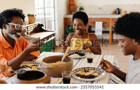 Brazilian family gathering around the table for a traditional meal, sharing laughter and smiles. The table is filled with delicious dishes and the best of Brazilian cuisine, couve and feijoada. Royalty-Free Stock Photo #2357055541