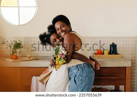 Daughter surprises her mom with a heartfelt gift of flowers in the kitchen, sharing a loving moment and bringing happiness to their home. Perfect for Mother's Day or any special occasion. Royalty-Free Stock Photo #2357055639