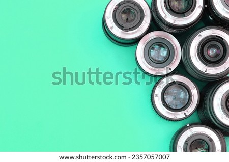 Several photographic lenses lie on a bright turquoise background. Space for text