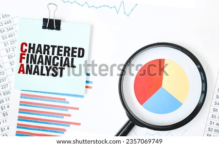 Green card on the white notepad and magnifier on the financial documentation. Text CHARTERED FINANCIAL ANALYST. Business concept