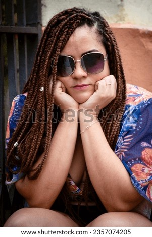 Portrait of pretty woman wearing sunglasses with braided hair leaning against iron railing. Calm person. Pelourinho, Brazil.