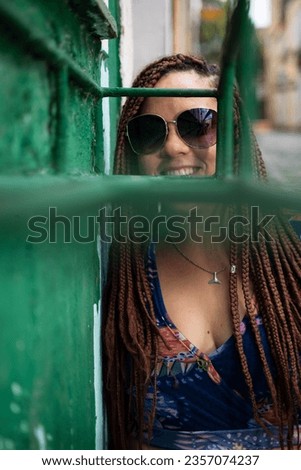 Portrait of a pretty woman wearing sunglasses looking at the camera through a green iron railing. Pelourinho, Brazil.