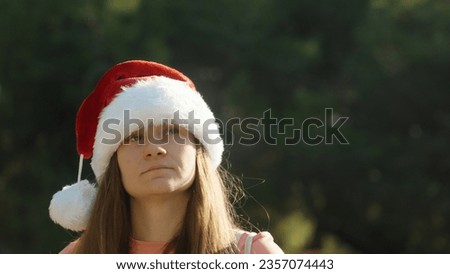A young woman in a red Christmas hat walks against the background of a green forest. A warm Christmas.