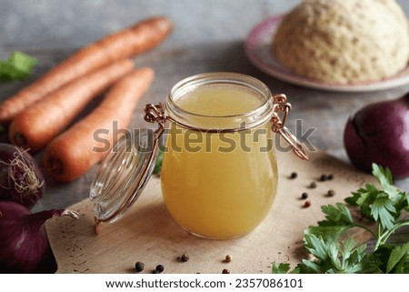 A jar of chicken bone broth on a rustic table with fresh veggies
