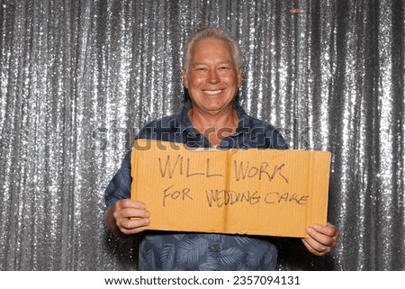 Photo Booth. Will Work For Wedding Cake. A man holds a carboard sign that reads WILL WORK FOR WEDDING CAKE while waiting for his pictures to be taken in a Photo Booth at a Wedding or Party. Wedding. 