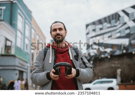 Portrait of a young man wearing headphones on a city background. A handsome guy with big headphones and stylish casual clothes on a city street