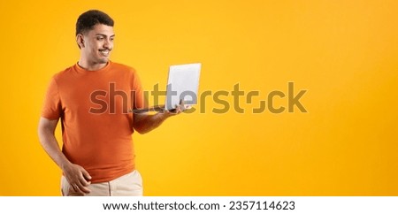 Happy brazilian man using laptop computer working online or websurfing posing on yellow background, panorama, copy space. Internet technology business and freelance career