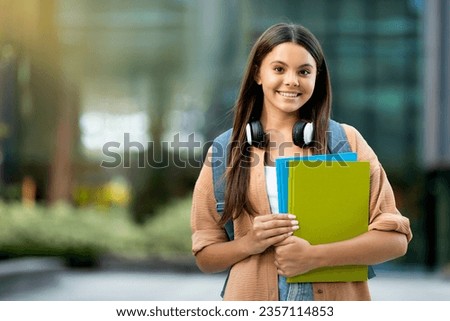 Positive pretty young woman student wearing casual outfit with backpack and notepads exercise books posing outdoor at university campus, smiling at camera, copy space. Students lifestyle Royalty-Free Stock Photo #2357114853