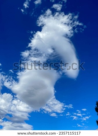 Interesting unusual funny shape of large high white clouds on a beautiful blue sky in a hot summer sunny day looks like a person as a nice relaxing background.
