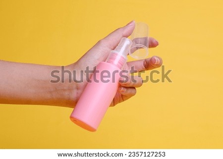 Female hand hold empty mockup cosmetic bottle on yellow background. 