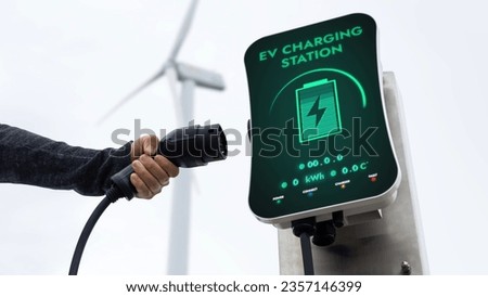 EV charger from EV car charging station in nature and wind turbine farm reducing CO2 emission. Technological advancement of alternative energy sustainability and EV car. Peruse