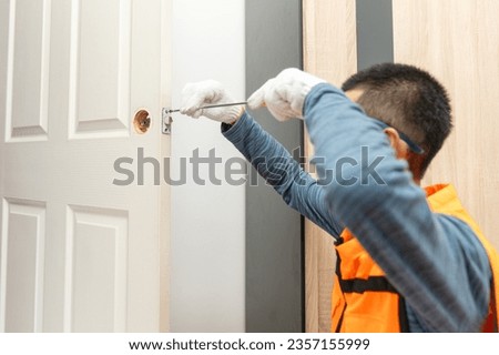 Asian professional locksmith installing or repairing a door knob with screw drive or cordless drill. Royalty-Free Stock Photo #2357155999