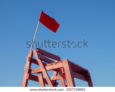 Red flag on a wooden platform. Flag as a symbol of danger. Bathing is prohibited. Beach on the sea. The concept of rescue work. Beach safety