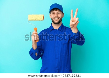 Painter caucasian man isolated on blue background smiling and showing victory sign