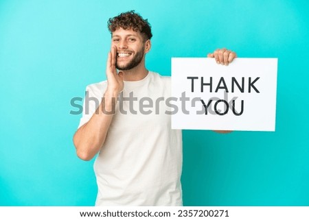 Young handsome caucasian man isolated on blue background holding a placard with text THANK YOU and shouting