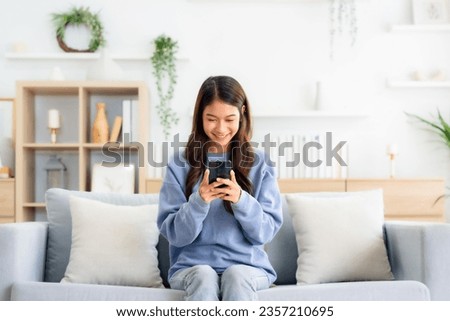 Happy young asian woman relax on comfortable couch at home texting messaging on smartphone, smiling girl use cellphone, chatting online message, shopping online from home Royalty-Free Stock Photo #2357210695