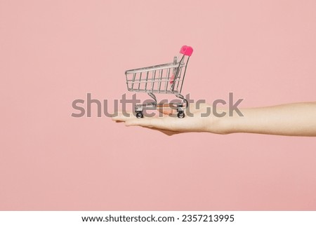 Close up cropped female holding in hand arm empty shopping cart isolated on pastel plain light pink color wall background studio. Black Friday sale buy day concept. Copy space advertising mock up