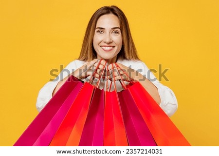 Young smiling cheerful fun cool woman wear white casual clothes hold in hand paper package bags after shopping look camera isolated on plain yellow background studio. Black Friday sale buy day concept