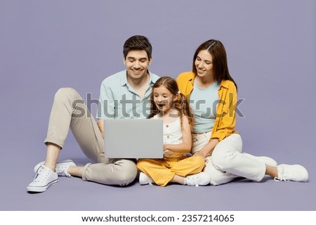 Full body young IT parents mom dad with child kid daughter girl 6 years old wear blue yellow casual clothes sit hold work on laptop pc computer isolated on plain purple background. Family day concept