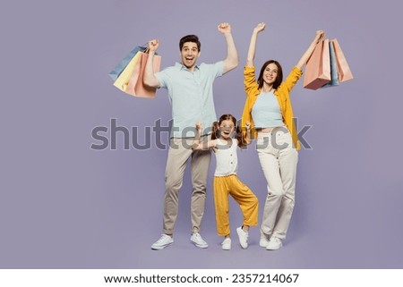 Full body young parents mom dad with child daughter girl 6 years old wear casual clothes hold shopping package bags do winner gesture isolated on plain purple background Black Friday sale day concept