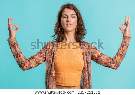 Keep calm down, relax, inner balance. Young woman breathes deeply with mudra gesture, eyes closed, meditating with concentrated thoughts, peaceful mind. Attractive girl isolated on blue background