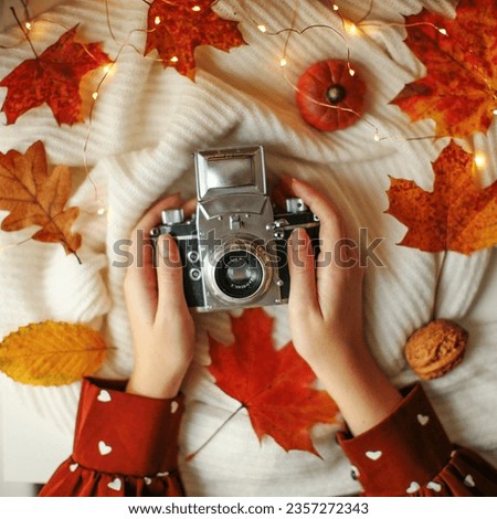 Autumn photo female hands holding retro vintage camera with yellow maple leafs closeup in warm day