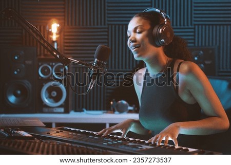 Young female artist recording a song in the studio, she is singing and playing the keyboard Royalty-Free Stock Photo #2357273537