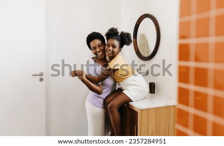 Joyful young girl holding hands with her loving mom by the bathroom sink. Mother and daughter, smiling and laughing, enjoying their special bond and a happy self-care routine in their home. Royalty-Free Stock Photo #2357284951