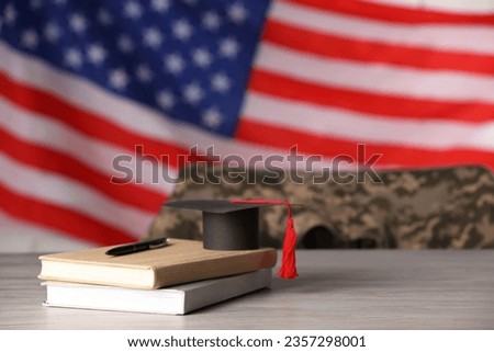Notebooks, mortarboard and pen on wooden table against flag of USA, space for text. Military education Royalty-Free Stock Photo #2357298001