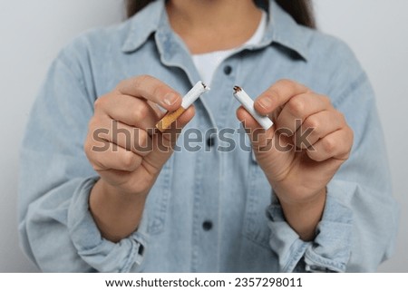 Stop smoking concept. Woman holding pieces of broken cigarette on light grey background, closeup