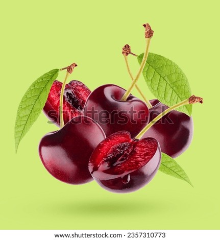 Bright red cherry with green leaves closeup levitation as art composition. Whole and piece fruits on colorful green background with shadow. Ripe fresh fruits for advertising, design, label product.