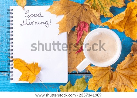 Coffee mug with bouquet of autumn fall leaves and flowers, notes good morning on turquoise blue wooden table, from above, cosy beautiful autumn breakfast, vintage card, top view, flat lay