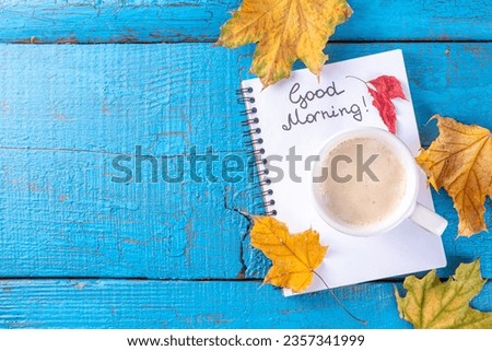 Coffee mug with bouquet of autumn fall leaves and flowers, notes good morning on turquoise blue wooden table, from above, cosy beautiful autumn breakfast, vintage card, top view, flat lay