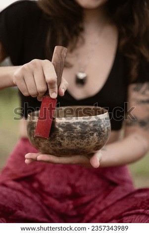 Tattooed woman holding and playing a Tibetan singing bowl Royalty-Free Stock Photo #2357343989
