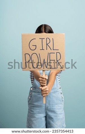 Protester woman holding recycled cardboard with girl power slogan. Unrecognizable teenage girl feminist with empowerment sign isolated on studio blue background. Women's rights concept. 