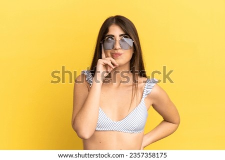 Young caucasian woman in swimsuit in summer holidays isolated on yellow background thinking an idea