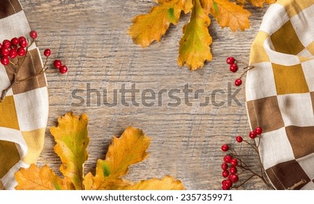 Oak branch with dry autumn leaves and rowan berries on a wooden table and autumn tablecloth