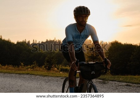 A fit male cyclist practicing on a gravel road at sunset. He is riding a gravel bike with a view of the mountains. Bucegi Mountains, Romania