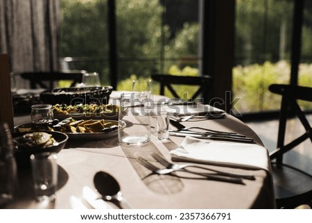 Luxurious Restaurant Table with shiny cutlery. Opulent Setting for Fine Dining Experience. High end restaurant. Romantic dinner in sunset light. Sunlight table. Vodka shot glass. Royalty-Free Stock Photo #2357366791