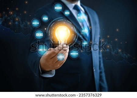 Businessman hand holding creative light bulb with icons brand data marketing plan ideas analyse solution creative innovative and development, on stock graph background. Business technology concept. 