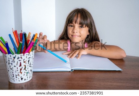 hobby, art and childhood concept - happy smiling girl with pencils and colors drawing picture over home room background
