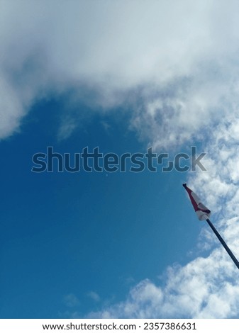 Red and white flag under blue sky and thin clouds