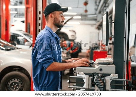 Standing by computer terminal. Auto mechanic working in garage. Repair service. Royalty-Free Stock Photo #2357419733