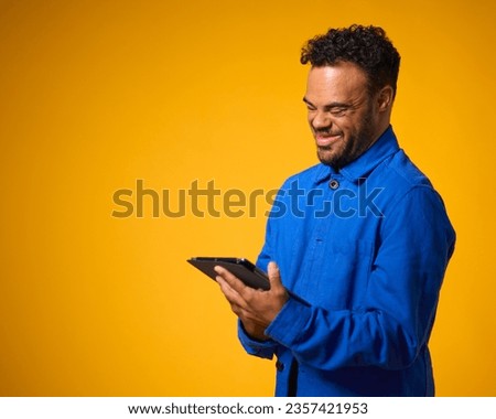 Studio Portrait Of Man With Down Syndrome Using Digital Tablet Against Yellow Background Royalty-Free Stock Photo #2357421953