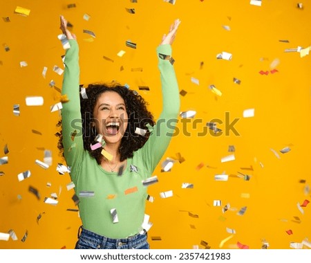 Studio Shot Of Excited Woman Celebrating Big Win Showered In Tinsel Confetti On Yellow Background Royalty-Free Stock Photo #2357421983