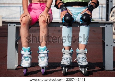 schoolgirls are sitting on a bench after roller skating. girls in protective equipment knee pads and a girl with a trauma on the skin after a fall Royalty-Free Stock Photo #2357443441