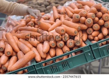 a photography of a pile of carrots in a green crate, grocery store display of carrots and potatoes in a green crate.
