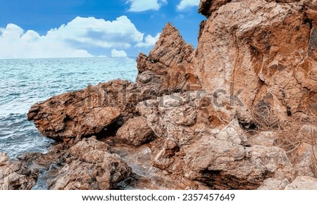 a photography of a rocky beach with a blue sky and some water, drop - off of a rock cliff into the ocean with a blue sky.