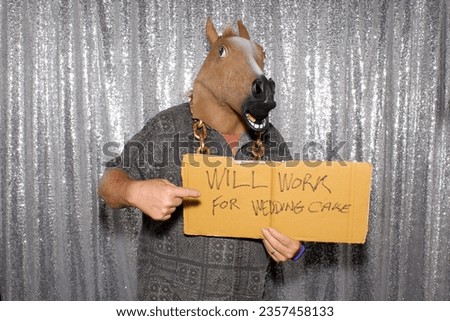 Photo Booth. Will Work For Wedding Cake. A man holds a carboard sign that reads WILL WORK FOR WEDDING CAKE while waiting for his pictures to be taken in a Photo Booth at a Wedding or Party. Wedding. 