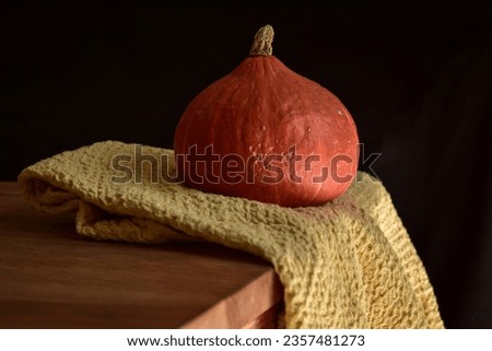 A bright orange pumpkin placed on top of a wooden table with a yellow kitchen cloth